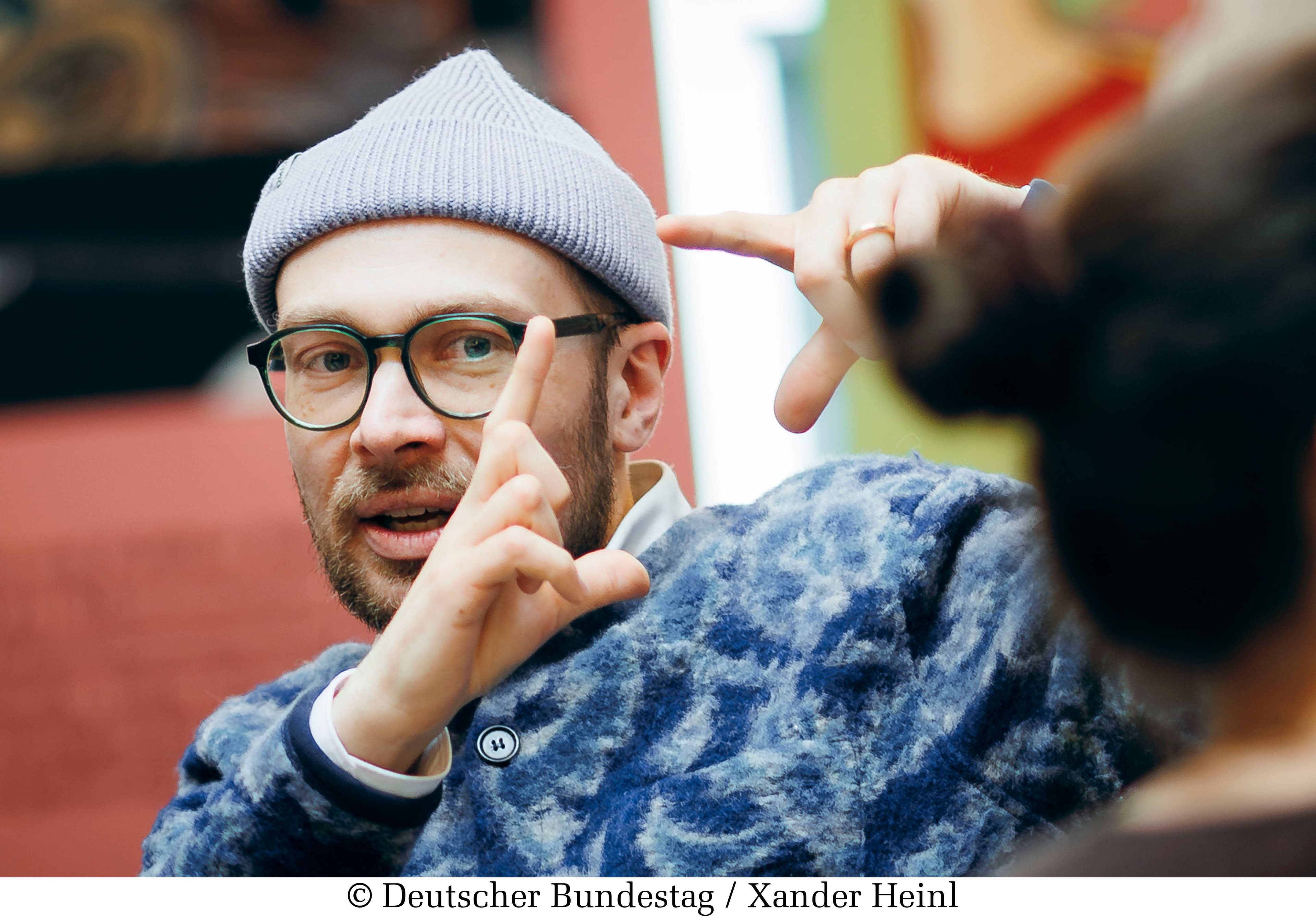 Simon Schwartz im Pullover mit Mütze im Gespräch gestikulierend