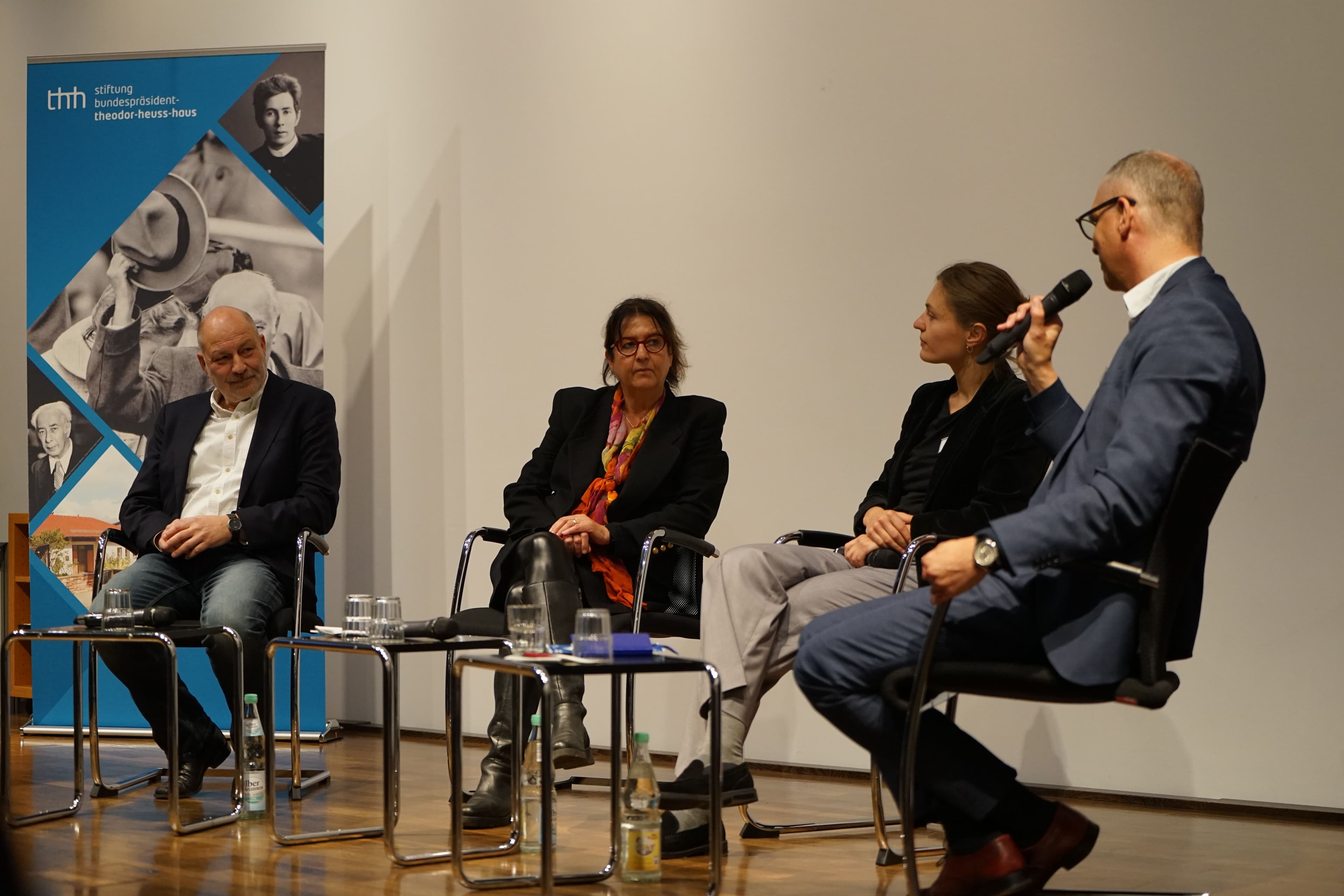 Drei Personen sitzen auf Sesseln und diskutieren vor einem Publikum.