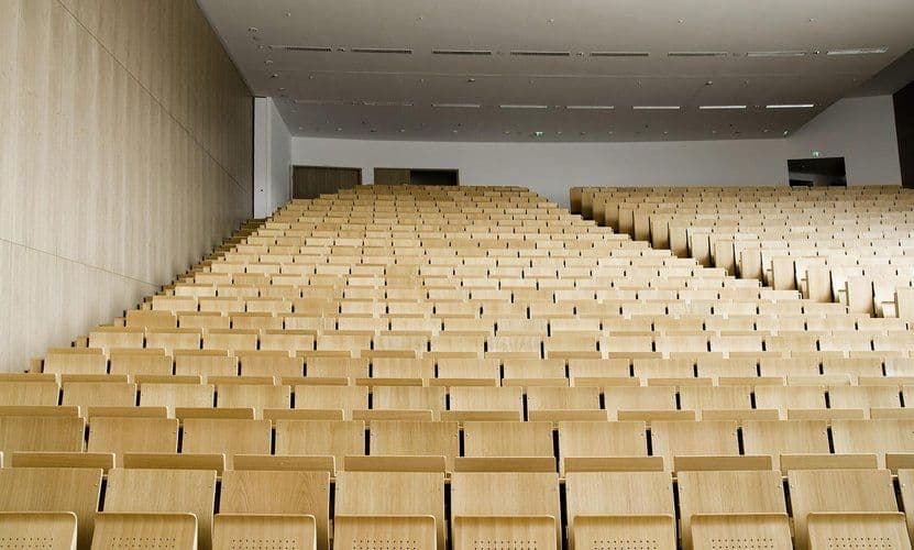 Ein leerer, modern gestalteter Hörsaal mit aufsteigenden Reihen heller Holzstühle und klarem, minimalistischem Design.